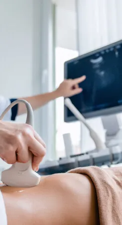 A doctor performing an abdominal ultrasound while pointing at the scan on a monitor.