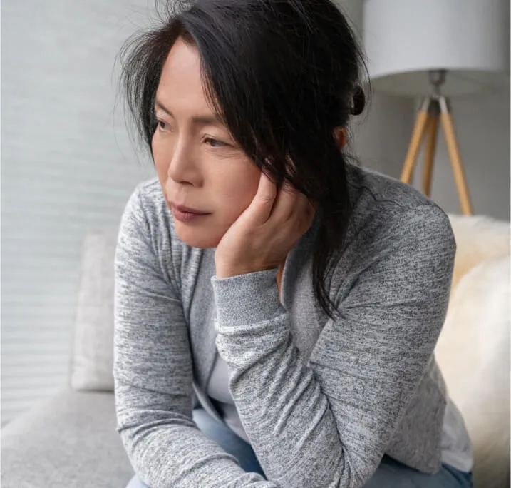 A middle-aged woman sitting on a couch looking downward with a worried expression.